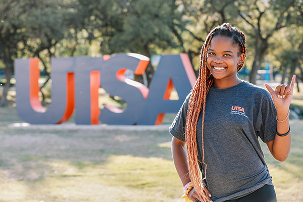 Smiling student standing in front of the UTSA sign on campus